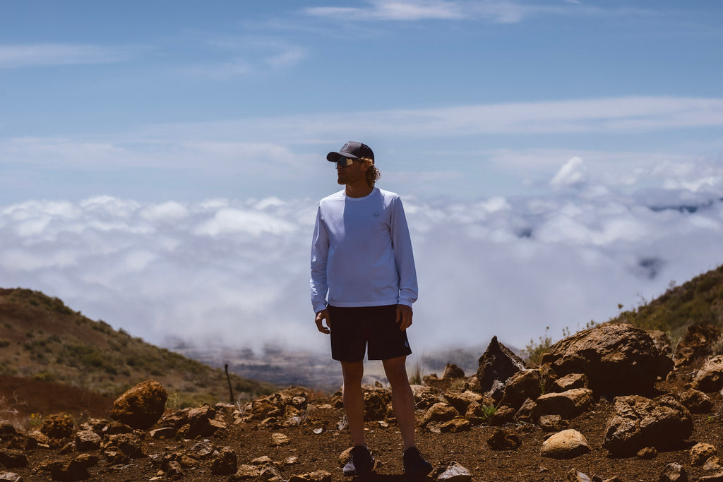 Eric Lagerstrom standing above the clouds on a barren rocky mountain wearing the Foreign Rider FR. Performance Long Sleeve T-Shirt