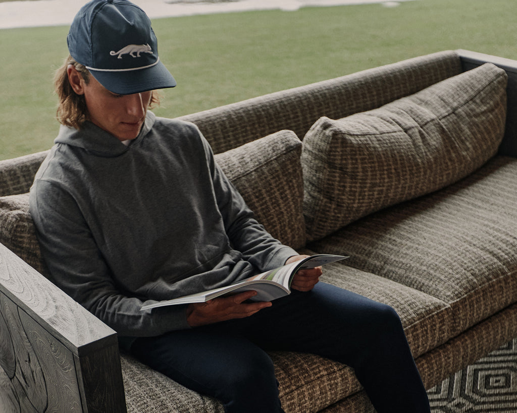 Man at Grove XXIII golf course sitting on a couch reading a magazine wearing Foreign Rider Co Performance Hooded Pullover