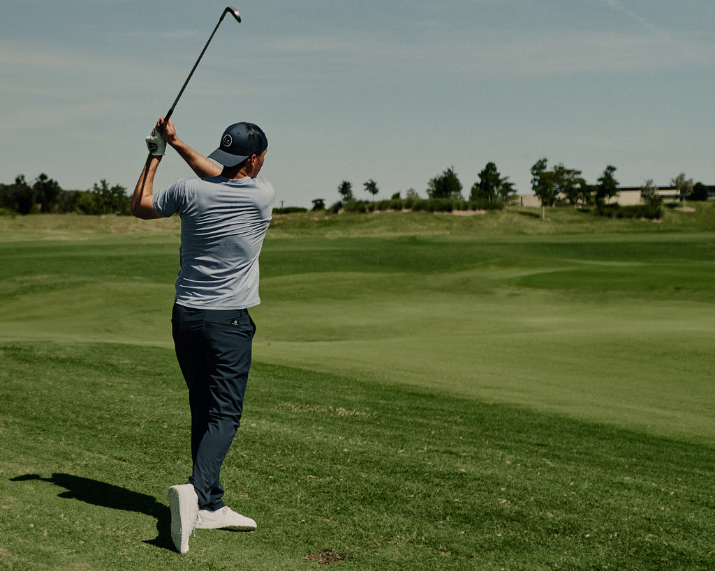 Man on Grove XXIII golf course looking at his golf ball as he finishes his swing wearing Foreign Rider Co Performance Pants