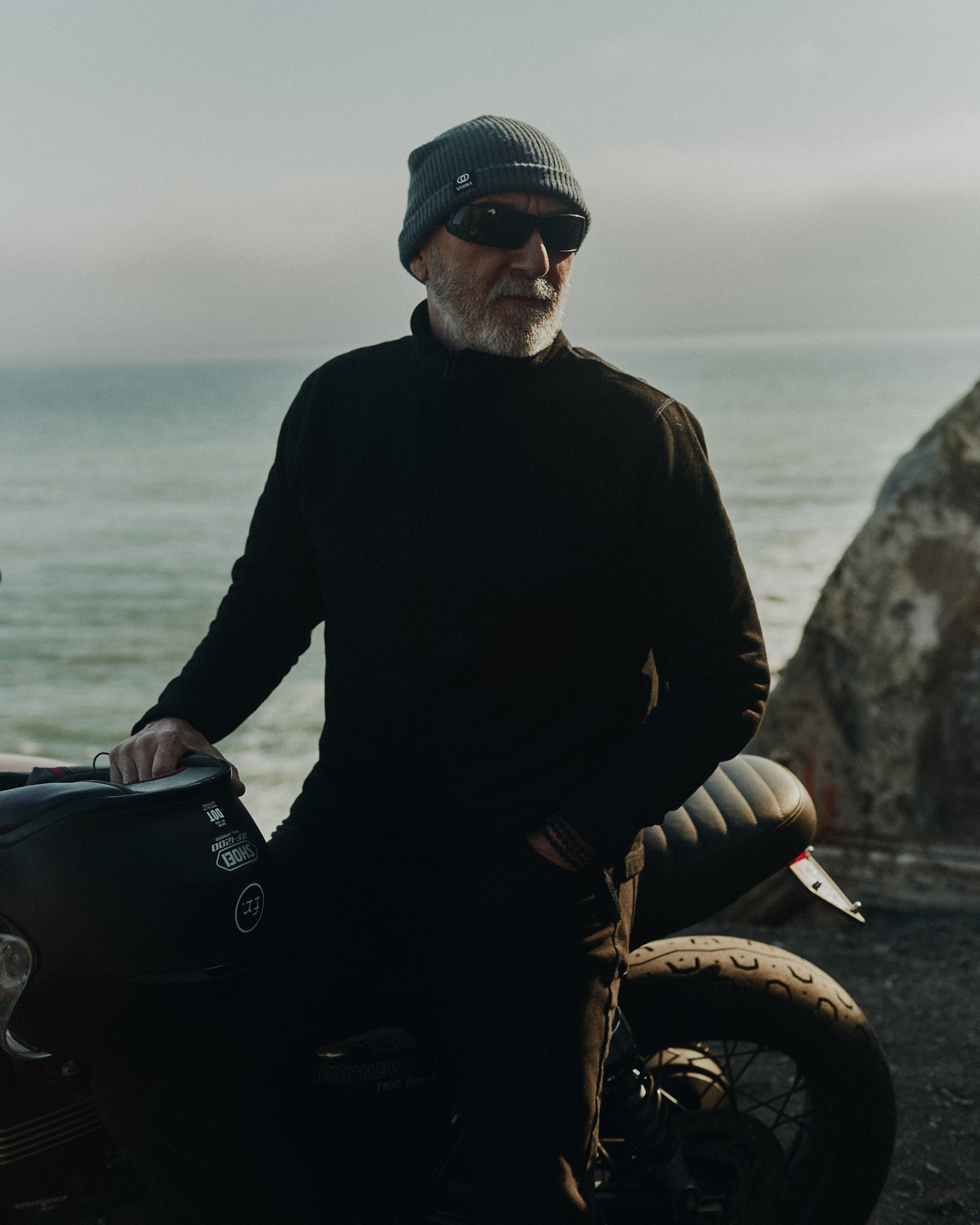 Ralph Dunning sitting on a vintage Triumph motorbike overlooking the Pacific ocean wearing the Foreign Rider Quarter Zip Sweatshirt