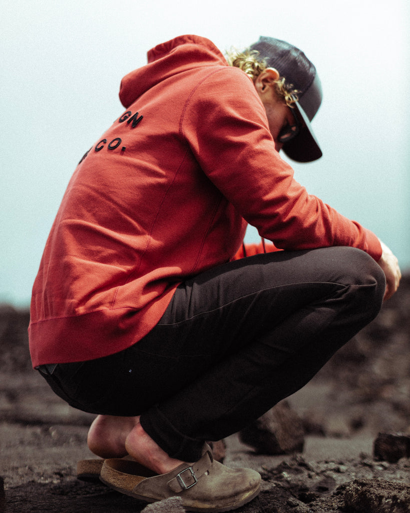 Eric Lagerstrom bending down looking at lava rocks wearing Foreign Rider Co. sweater and 5 pocket pant