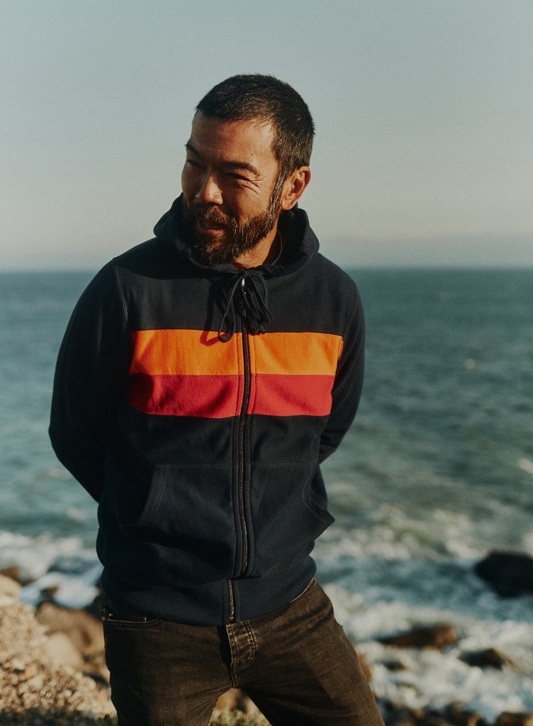 Man standing on a cliff overlooking the Pacific ocean wearing the Foreign Rider Striped Full Zip Hooded Sweatshirt