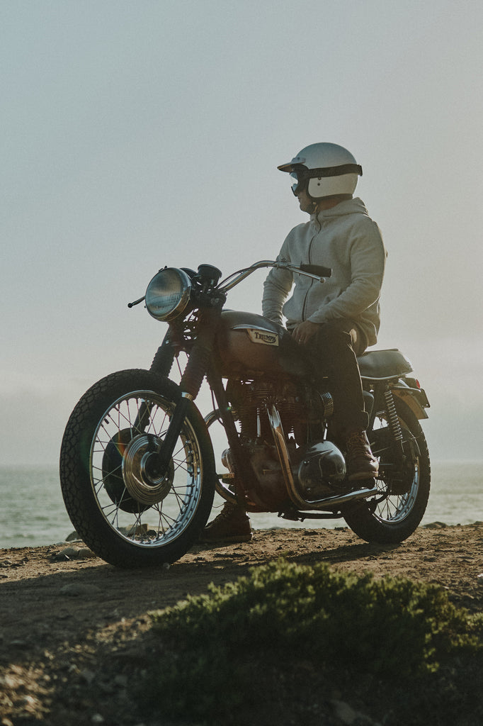 Angled view of man on idle Triumph motorcycle overlooking ocean