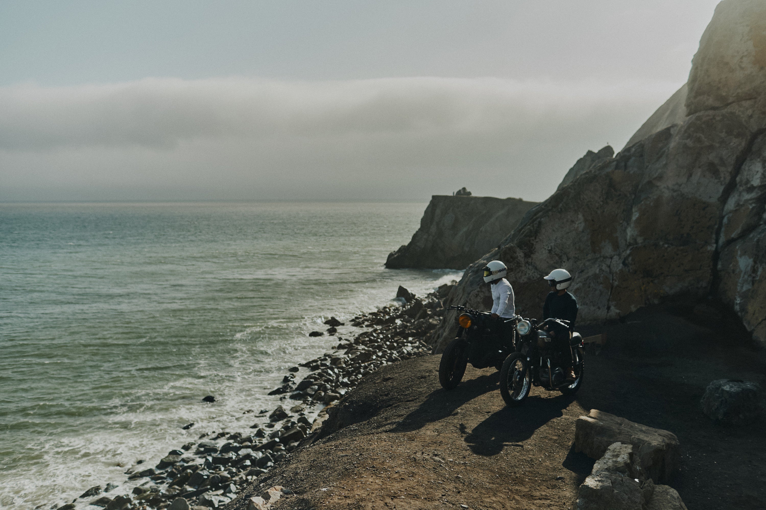 2 men sitting cliffside on idle vintage motorbikes overlooking the Pacific ocean wearing the Foreign Rider Supima Cotton Long Sleeve T-shirt