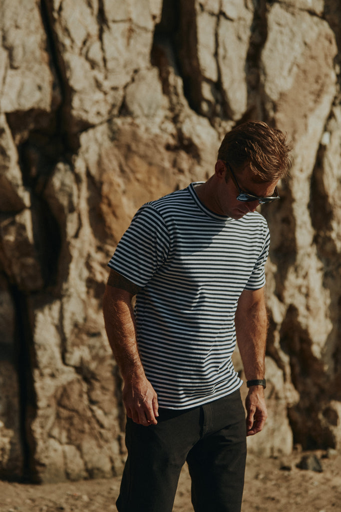 Man standing in front of a rock wall looking down wearing the Foreign Rider Vintage Stripe T-Shirt