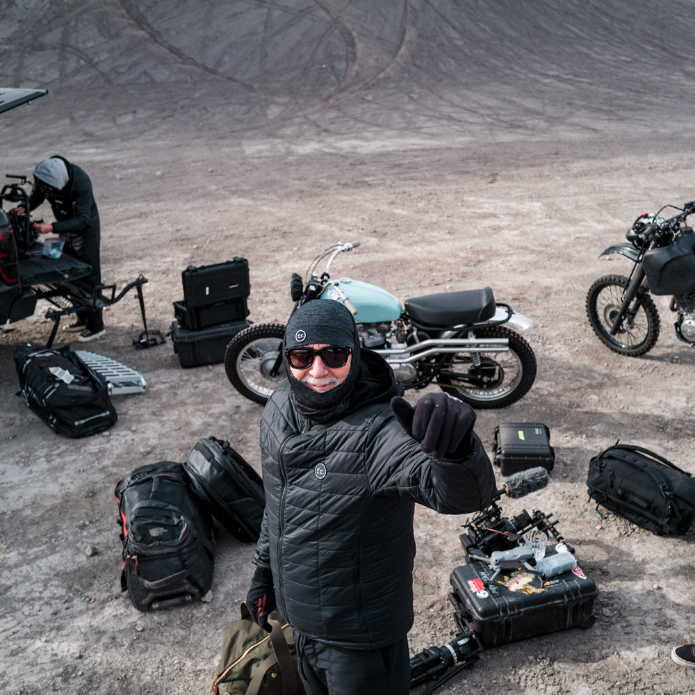 Man kneeling around camera equipment and bikes in desert giving thumbs up to the camera