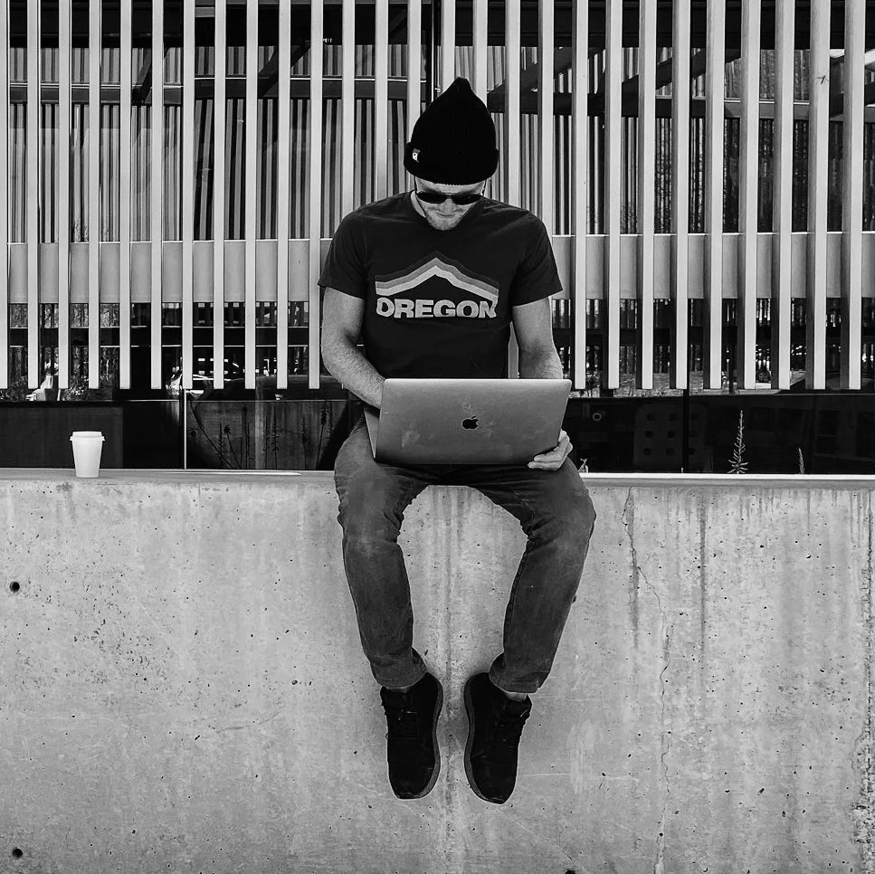 Eric Lagerstrom sitting on concrete wall typing on laptop