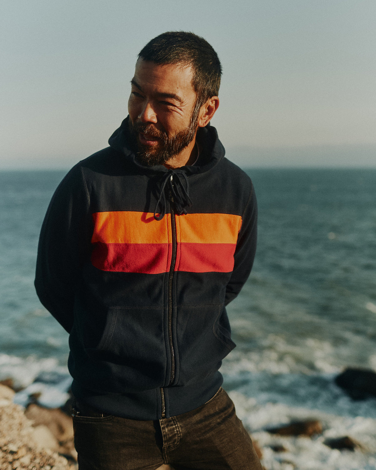 Man standing cliffside over the Pacific ocean wearing a Foreign Rider Striped Full Zip Hoodie