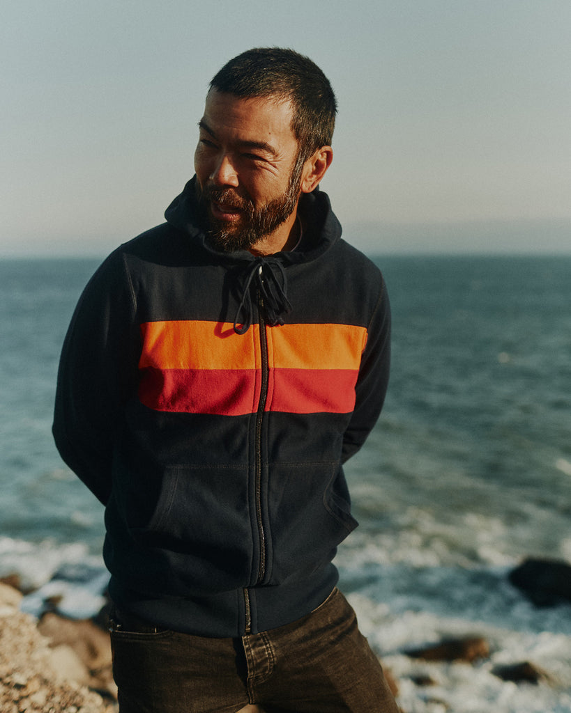 Man standing cliffside over the Pacific ocean wearing a Foreign Rider Striped Full Zip Hoodie