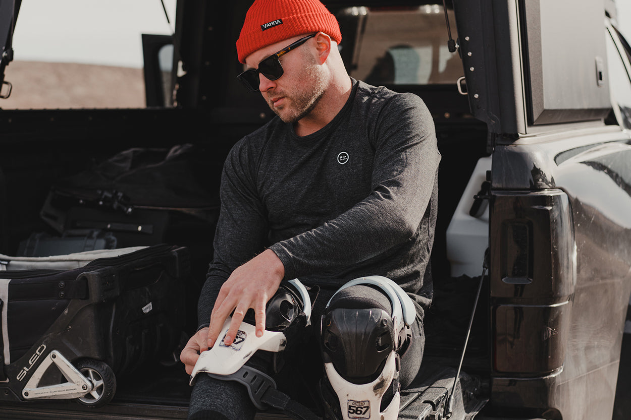 Man sitting on the back of a truck putting on moto gear wearing Foreign Rider clothing