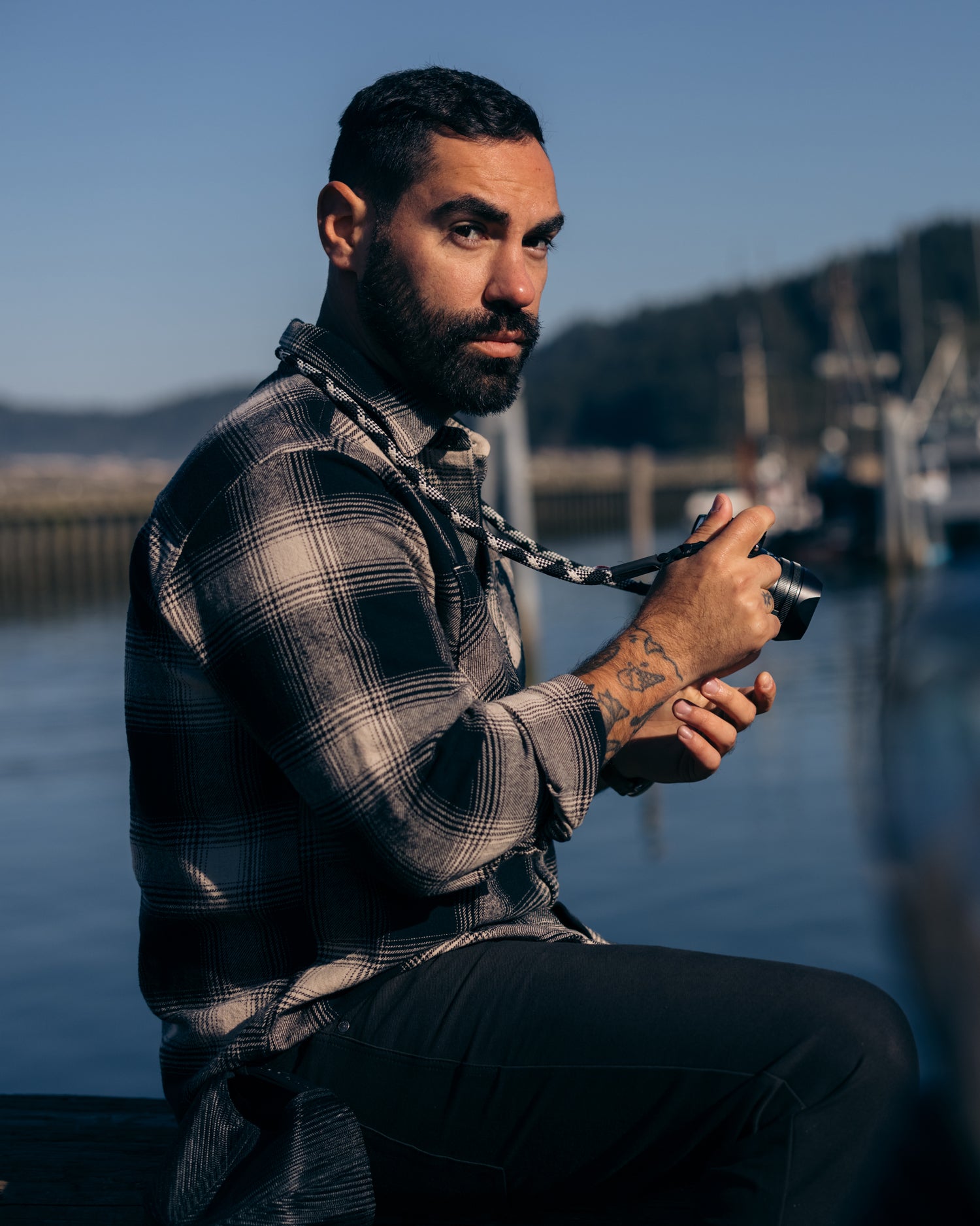 Man sitting on a pier holding a camera wearing Foreign Rider Co Black Flannel