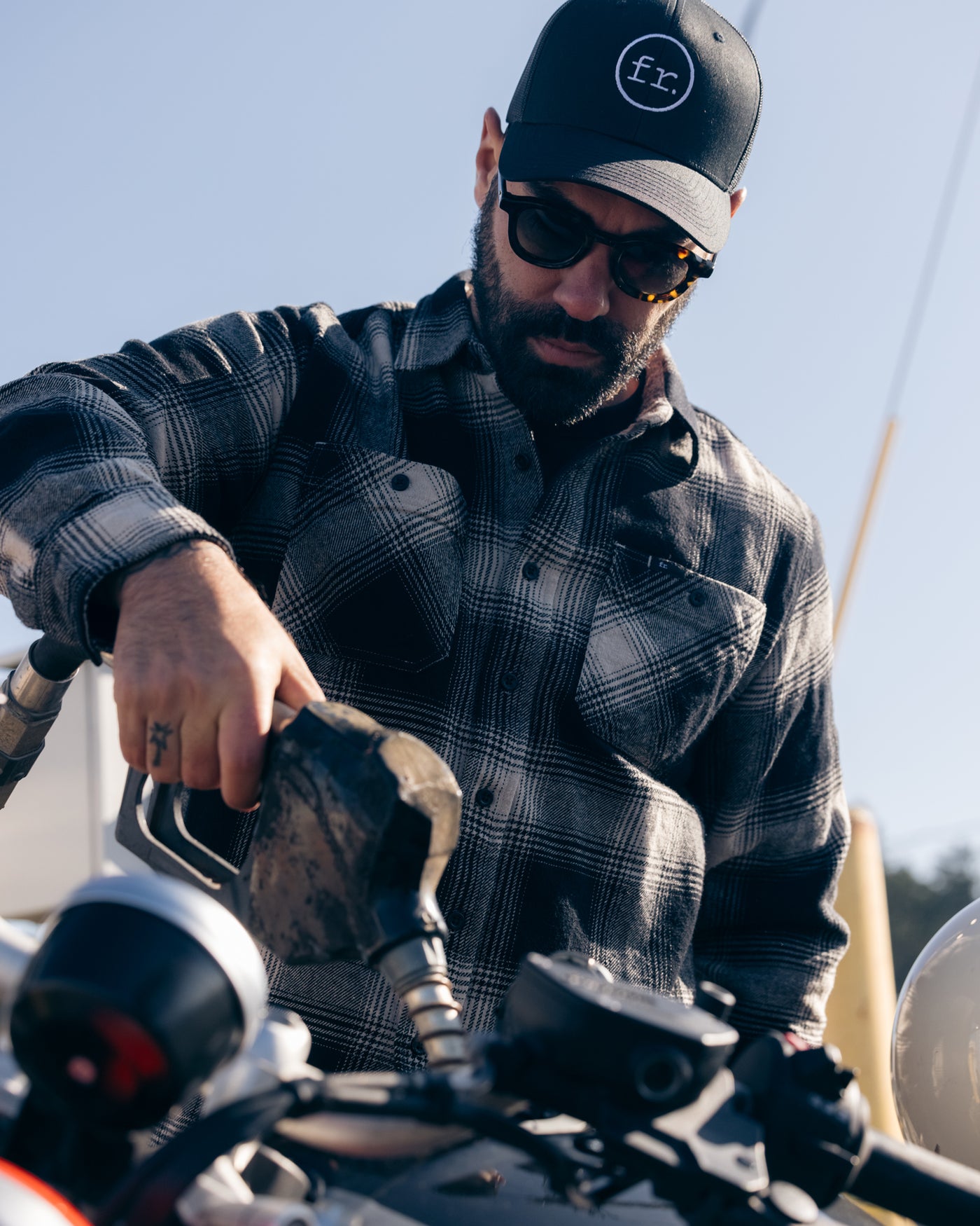 Man filling up BMW motorbike wearing Foreign Rider Co Hat & Black Flannel