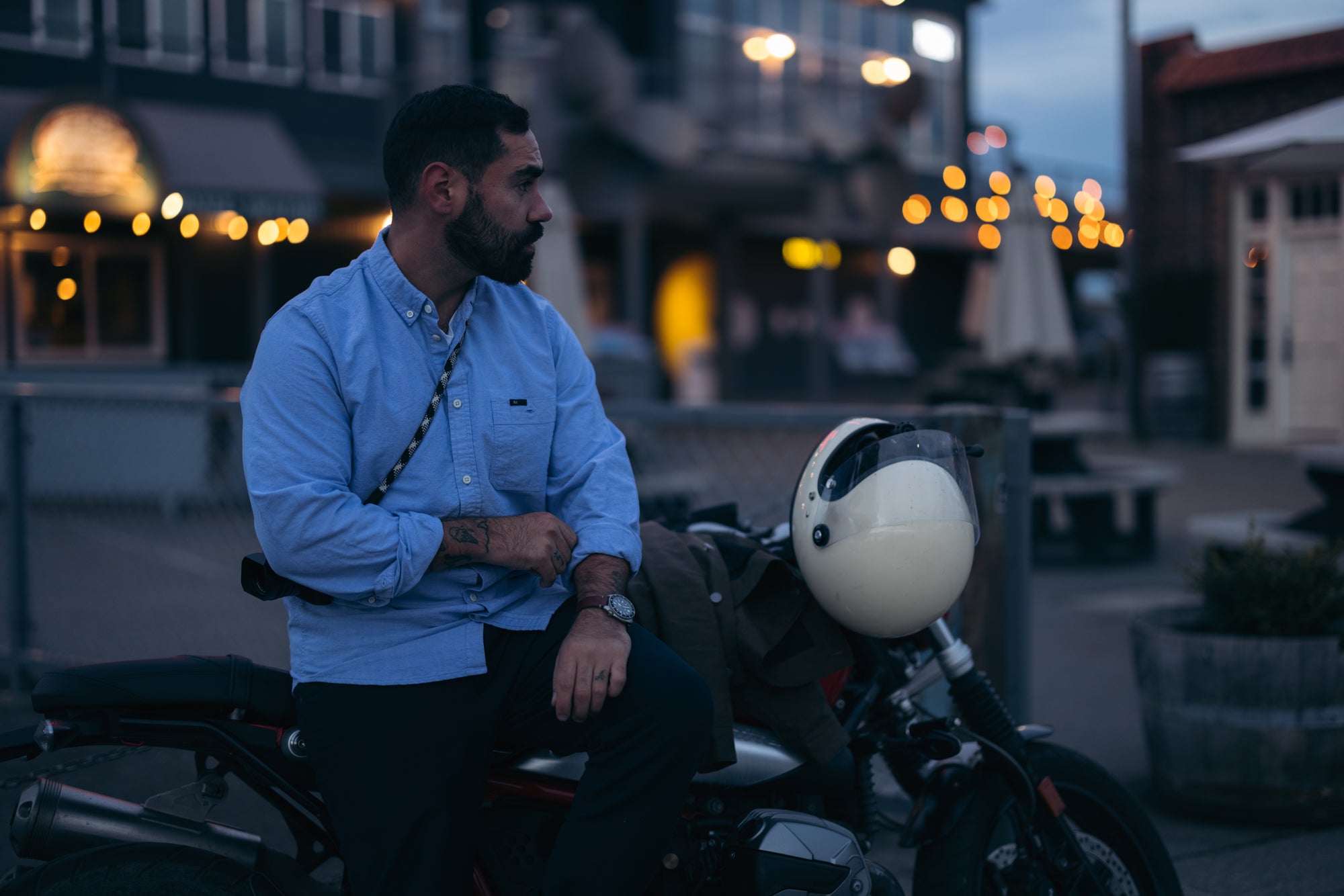 Man wearing Foreign Rider Co blue oxford button down sitting on side of BMW motorbike