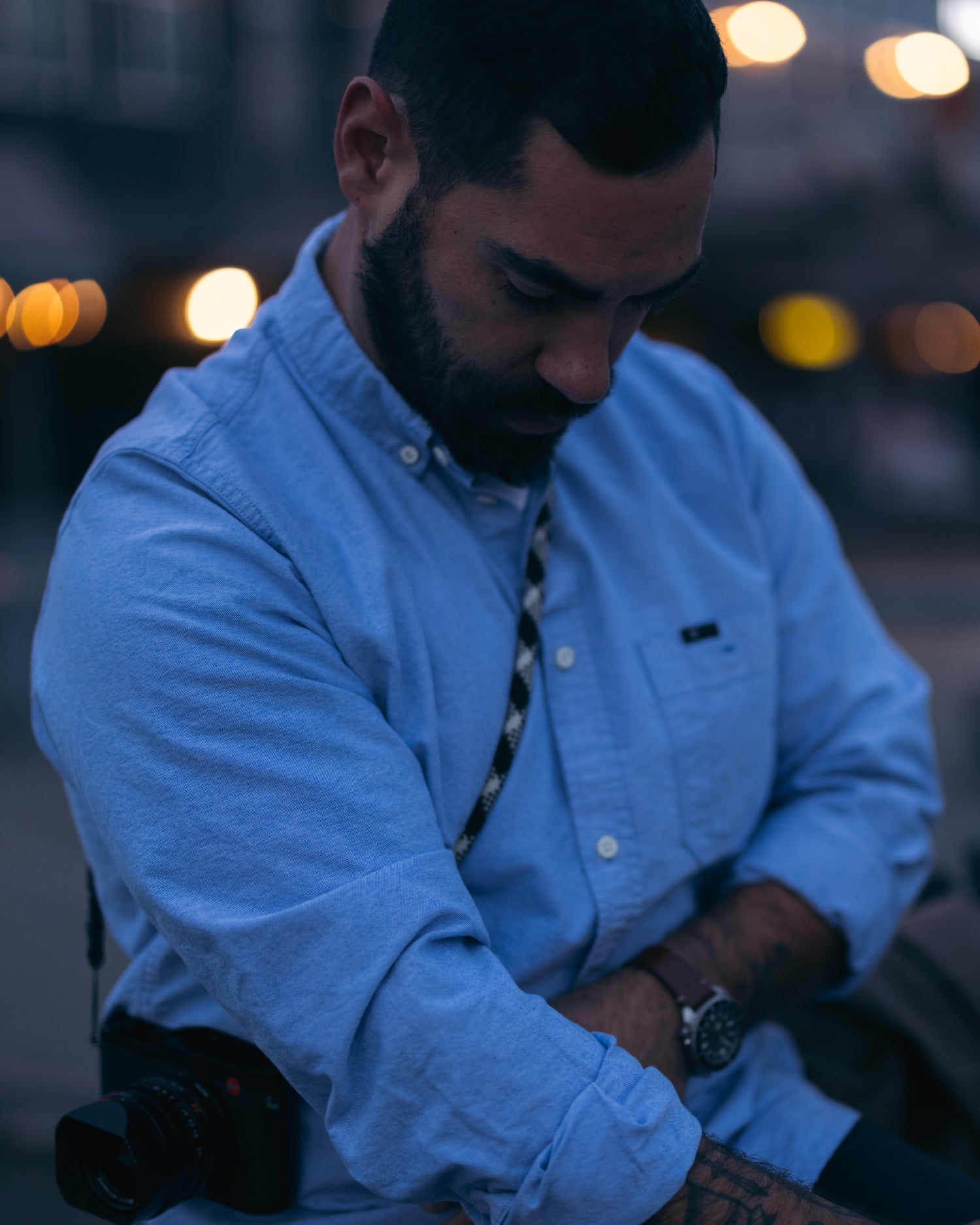 Man looking down adjusting sleeves & wearing Foreign Rider Co blue oxford button down