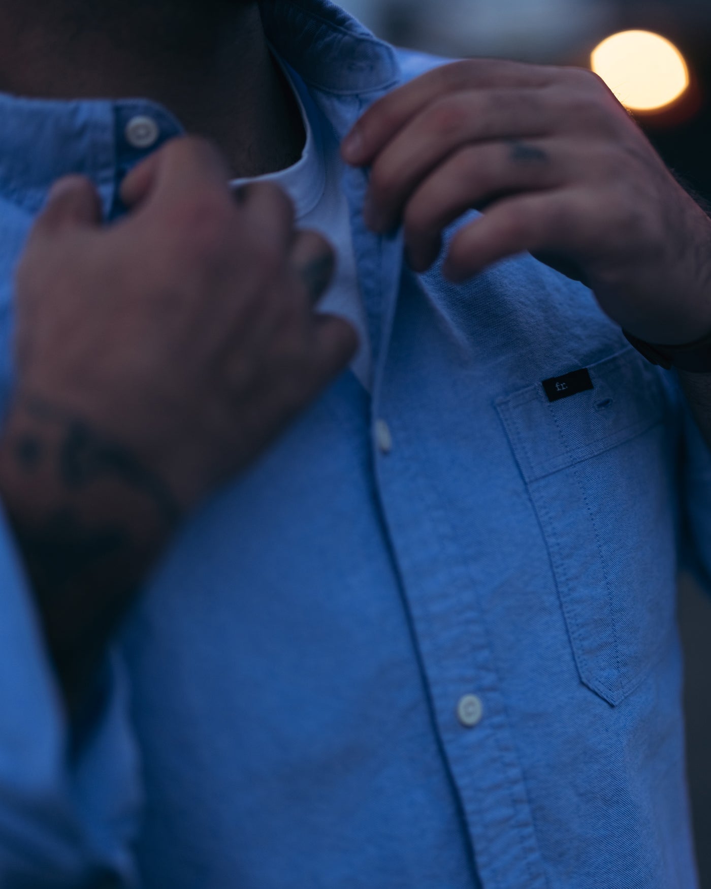 Man adjusting the buttons & collar of his Foreign Rider Co blue oxford button down