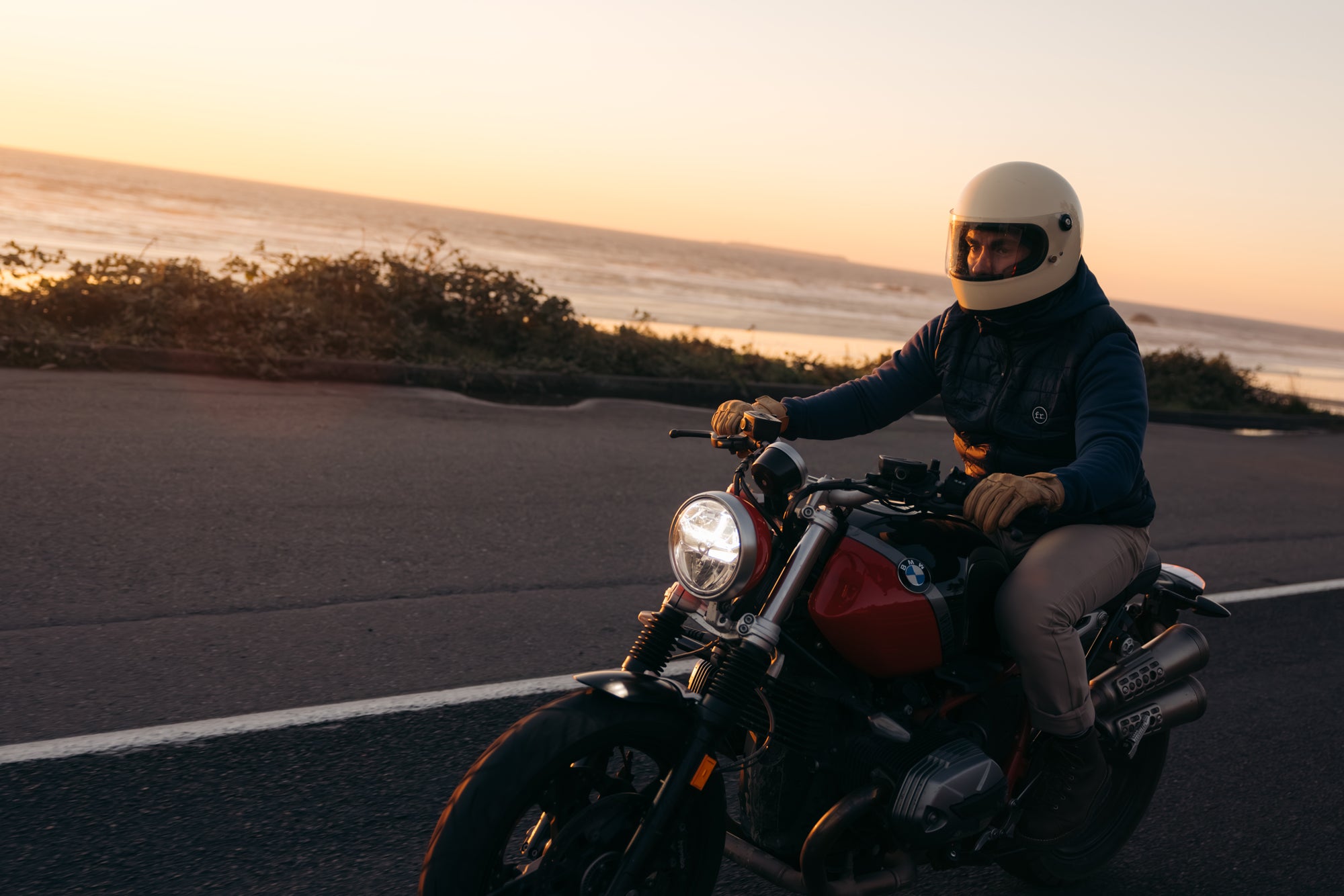 Man riding BMW Motobike on a road alongside ocean at sunset wearing Foreign Rider Insulated Vest