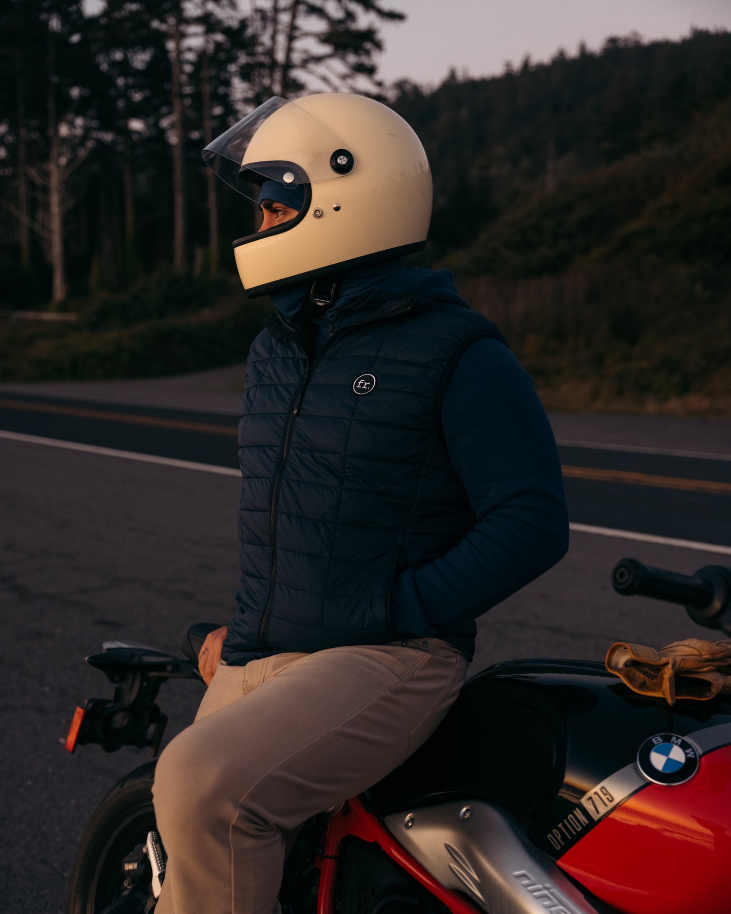 Side angle view of man sitting on side of BMW Motorbike wearing Foreign Rider Co Insulated Vest