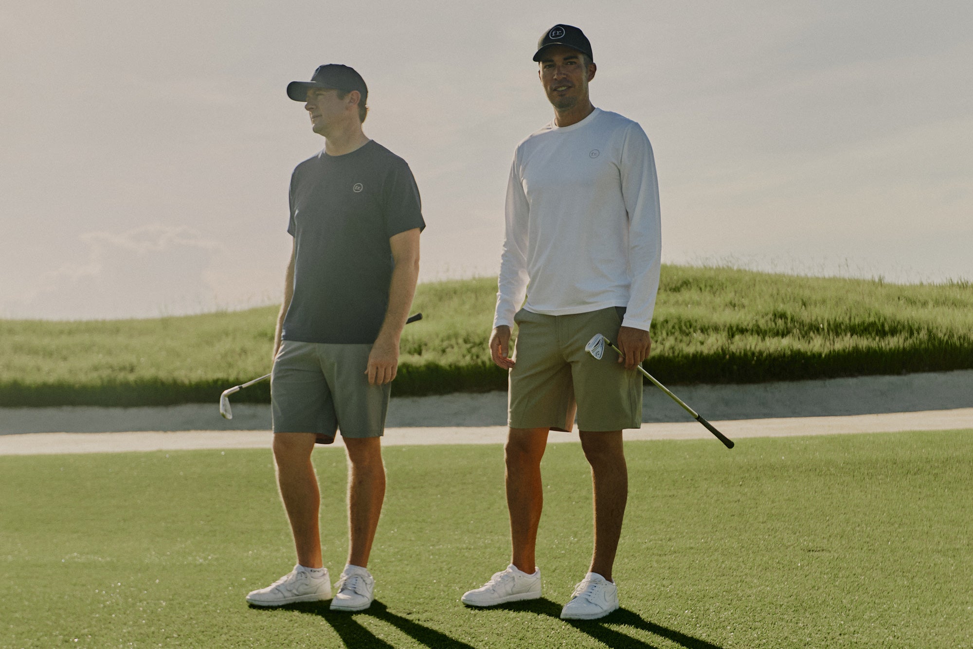 Two men on Grove XXIII golf course holding irons wearing Foreign Rider Performance Shorts