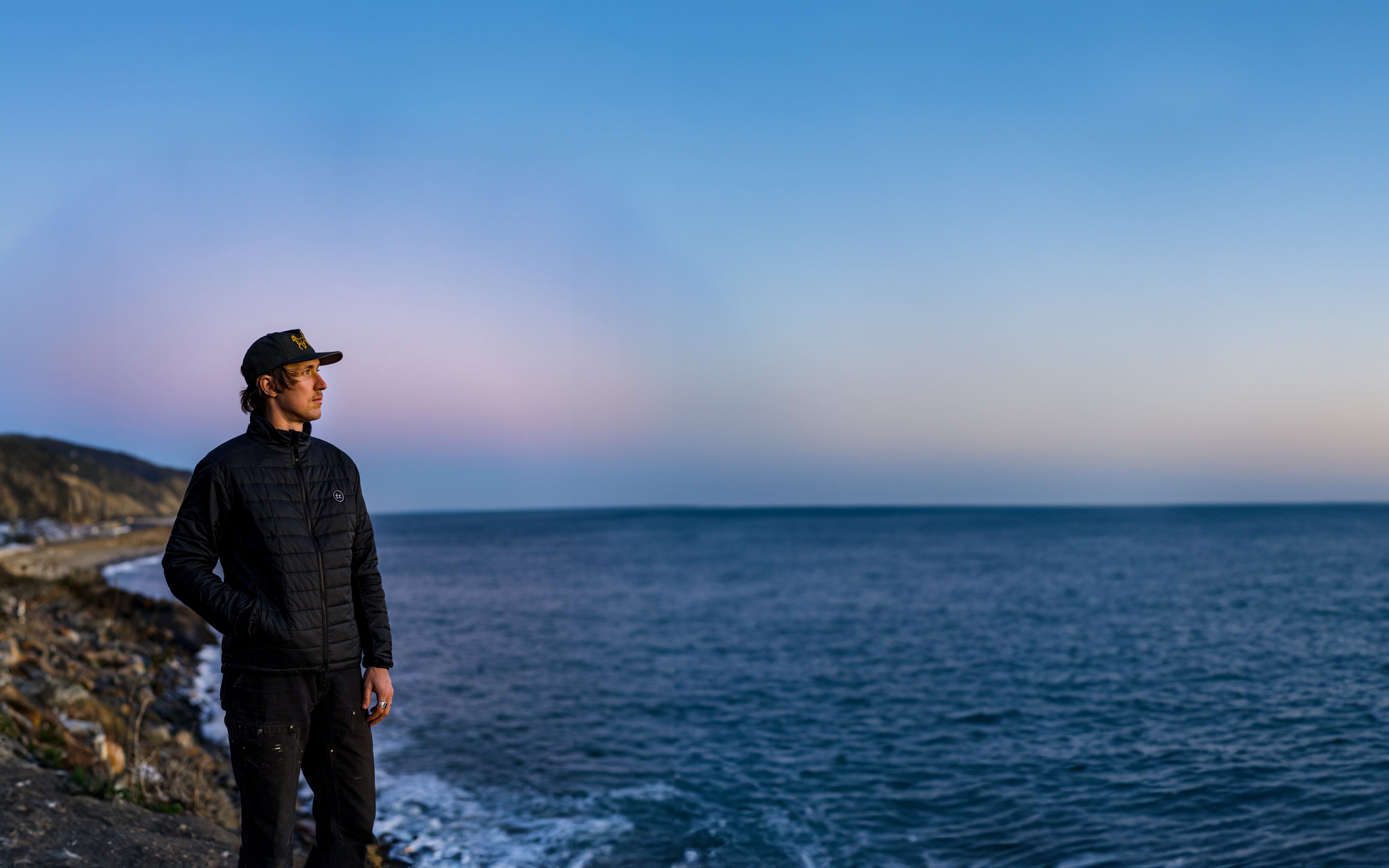 Man on the edge of a cliff during sunset looking out at the pacific ocean wearing Foreign Rider clothing