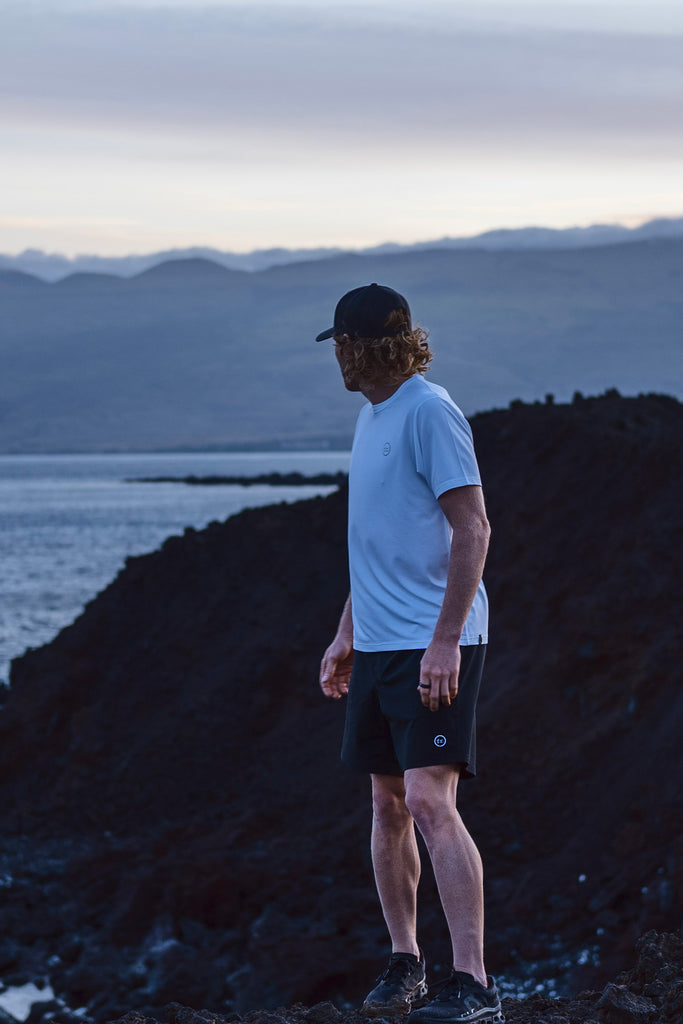 Eric Lagerstrom standing on a lava rock shoreline looking back at the ocean wearing the Foreign Rider FR. Performance Short Sleeve T-Shirt