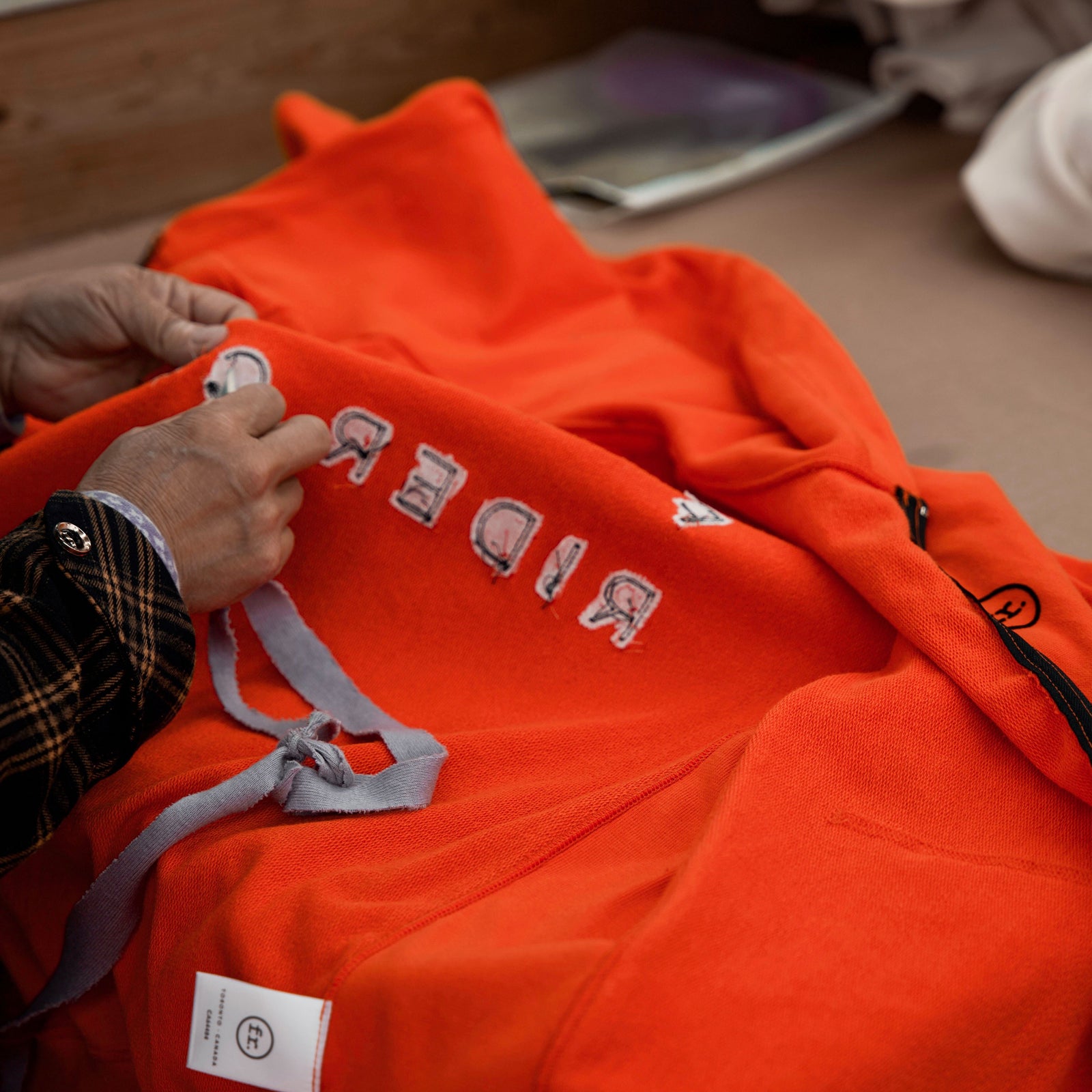 Man stitching the inside of an orange Foreign Rider sweater