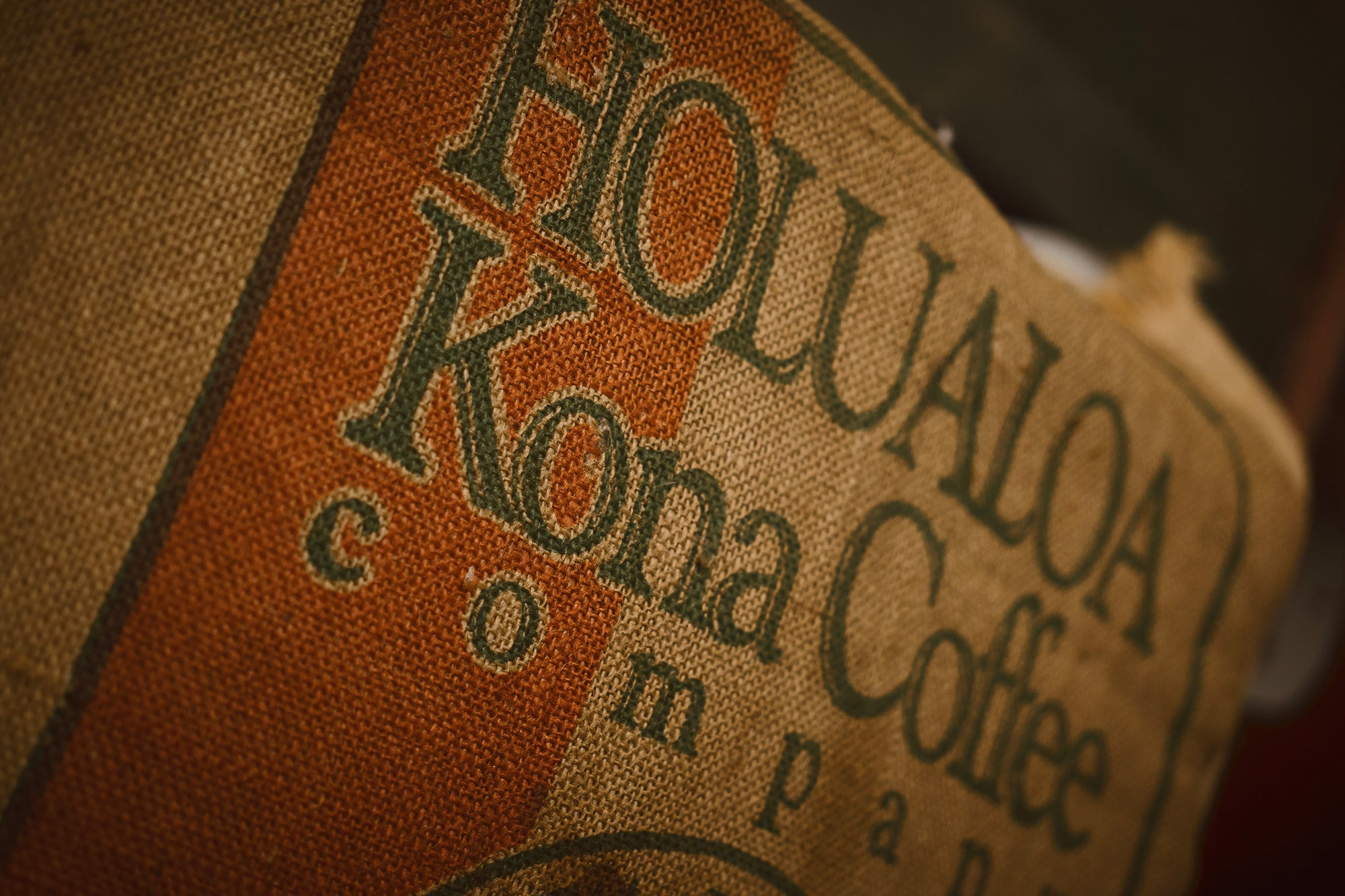 Close up shot of Hōlualoa Kona coffee company logo on a burlap sack holding coffee