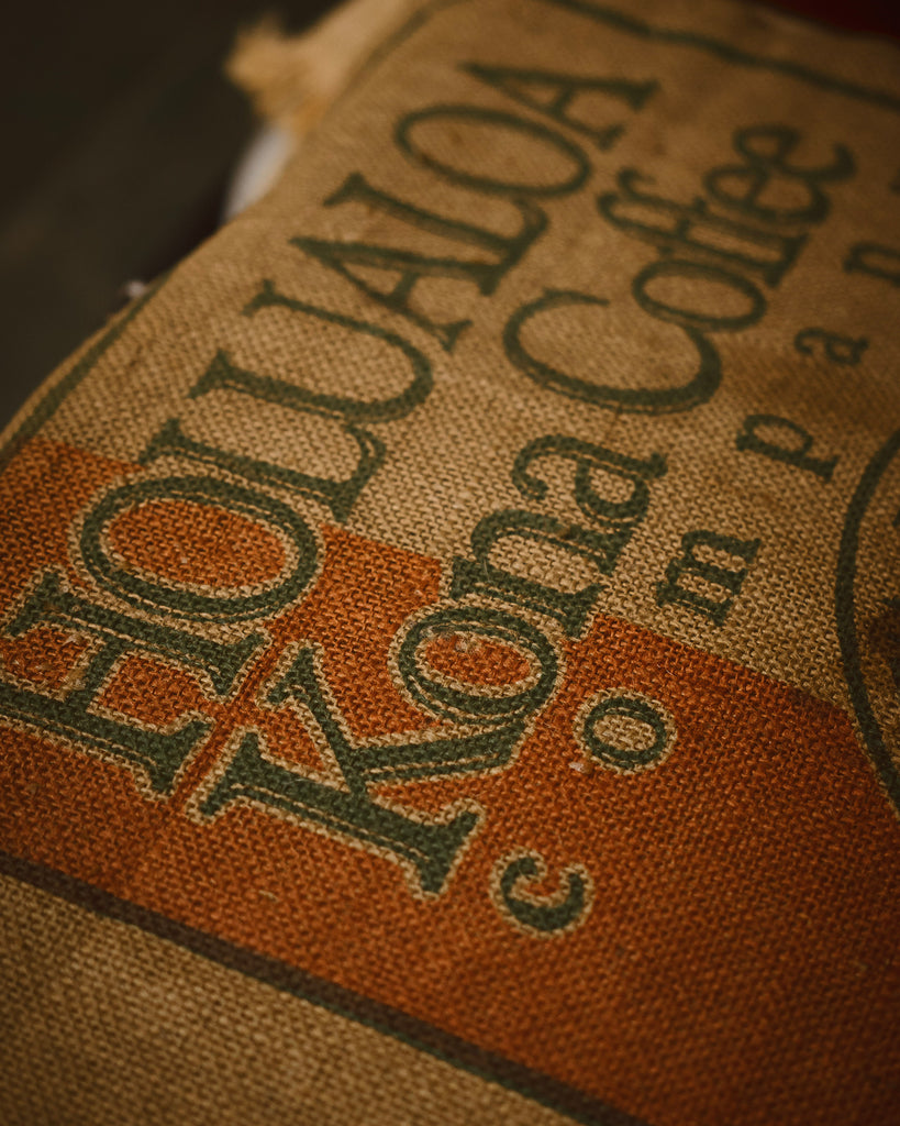 Close up shot of Hōlualoa Kona coffee company logo on a burlap sack holding coffee